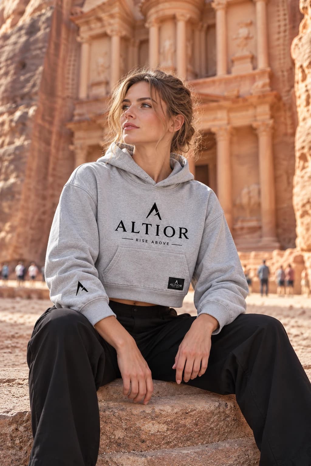Generated ALTIOR editorial: adult woman wearing carbon ash elevate crop hoodie in a Petra Treasury-inspired setting.